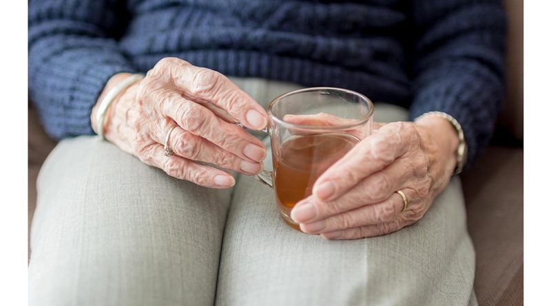 Kada nemokami teikiamos slaugos paslaugos namuose nuotraukoje moteris sėdi senose rankose laikydama stiklinį puodelį su arbata
